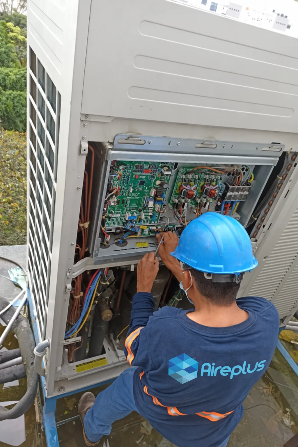 Técnico de Aire Plus con casco revisando la tarjeta electrónica de una unidad de aire acondicionado